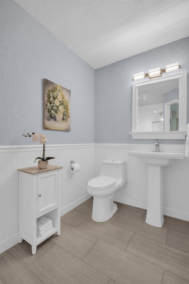 bathroom with a wainscoted wall, a textured ceiling, and toilet