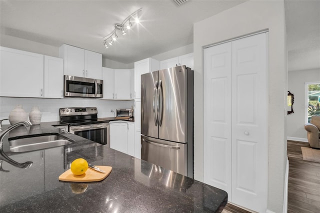 kitchen with white cabinets, dark stone countertops, stainless steel appliances, and a sink