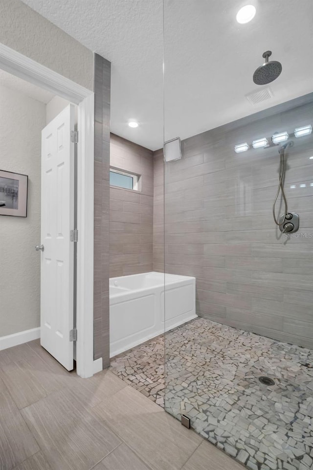 full bath with a tub to relax in, baseboards, and a tile shower