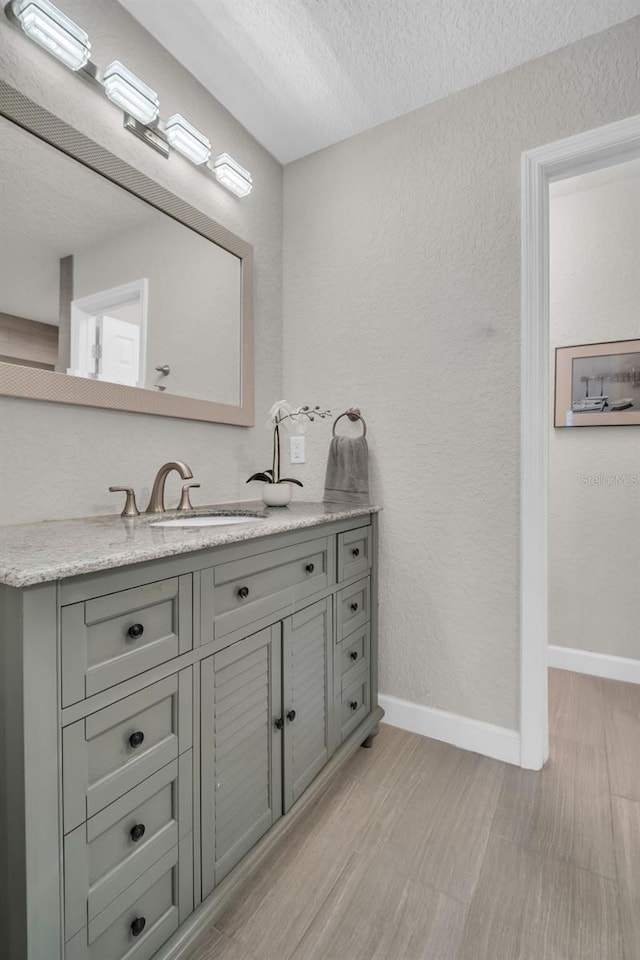 bathroom featuring a textured wall, vanity, baseboards, and a textured ceiling