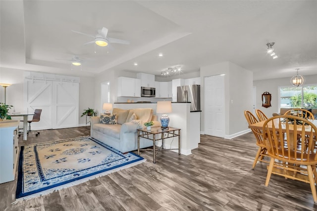 living room with ceiling fan with notable chandelier, dark wood-type flooring, a raised ceiling, and baseboards