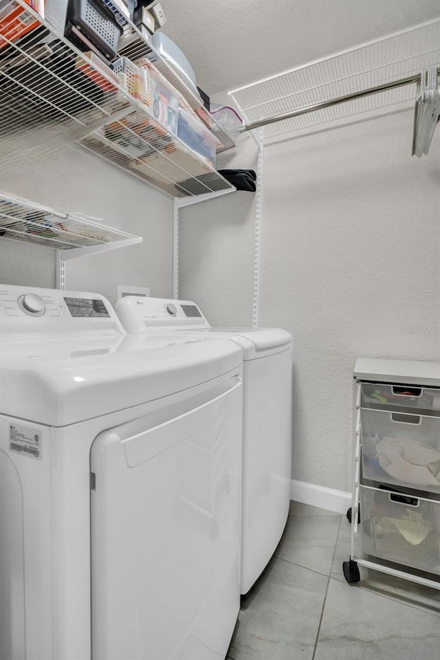 washroom featuring laundry area, washing machine and dryer, light tile patterned floors, and baseboards