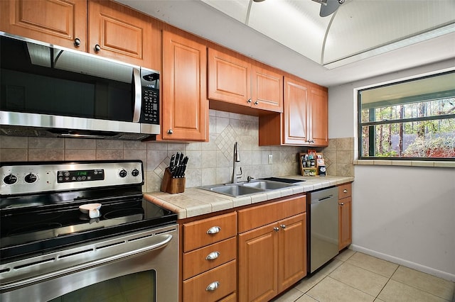 kitchen featuring light tile patterned floors, decorative backsplash, tile countertops, stainless steel appliances, and a sink