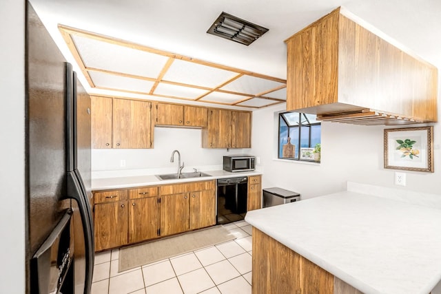 kitchen featuring brown cabinets, black appliances, a sink, light tile patterned flooring, and light countertops