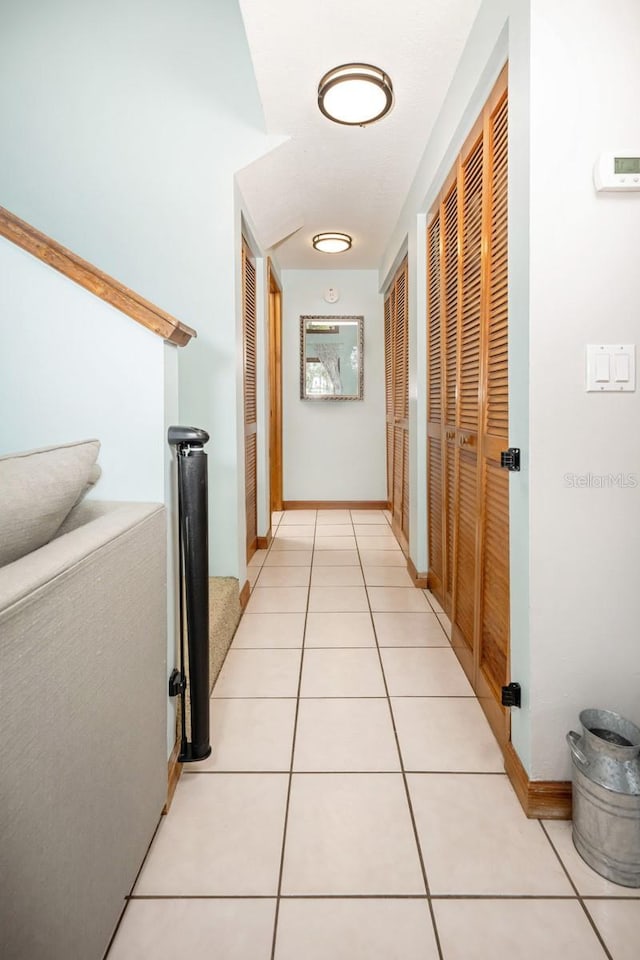 hall featuring stairway, baseboards, and light tile patterned flooring