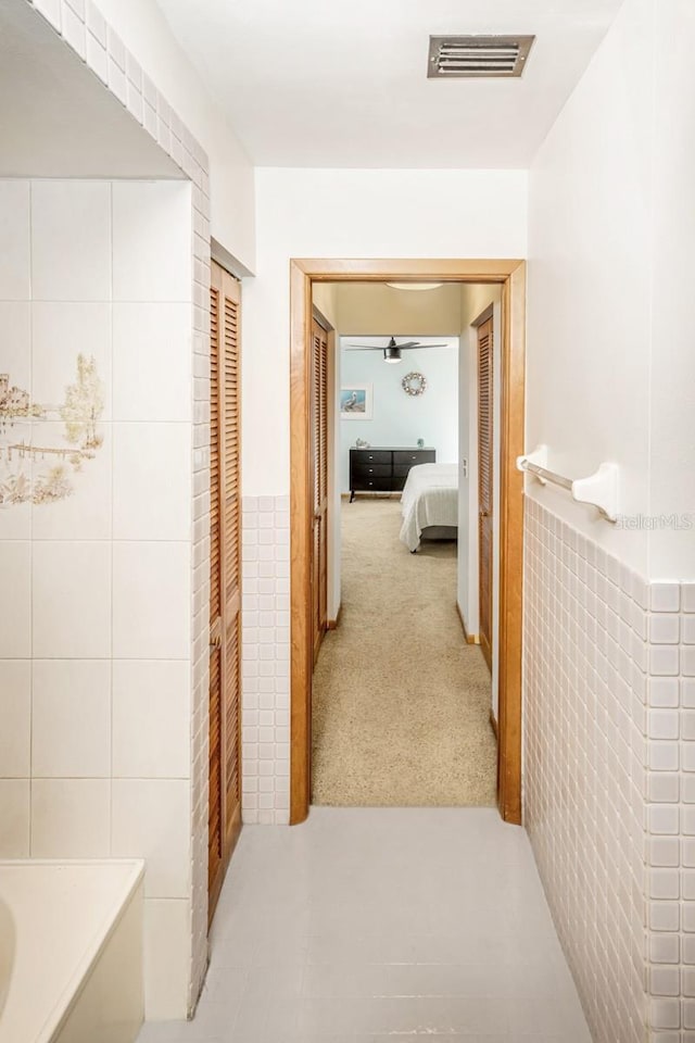 corridor with visible vents, carpet, and tile walls