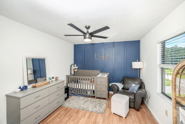 bedroom with a ceiling fan, a decorative wall, a nursery area, and light wood-style floors