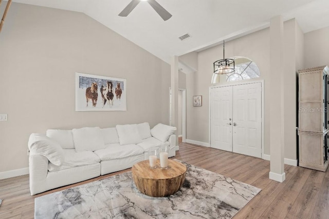 living area featuring high vaulted ceiling, light wood-type flooring, visible vents, and baseboards