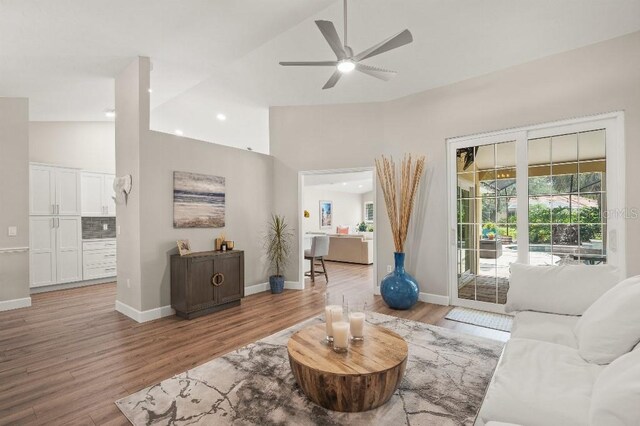 living area with a ceiling fan, high vaulted ceiling, baseboards, and wood finished floors