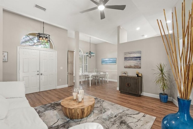 foyer featuring high vaulted ceiling, ceiling fan with notable chandelier, visible vents, and wood finished floors