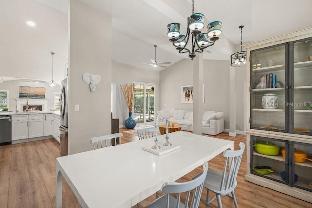 dining area with light wood finished floors, high vaulted ceiling, and ceiling fan with notable chandelier