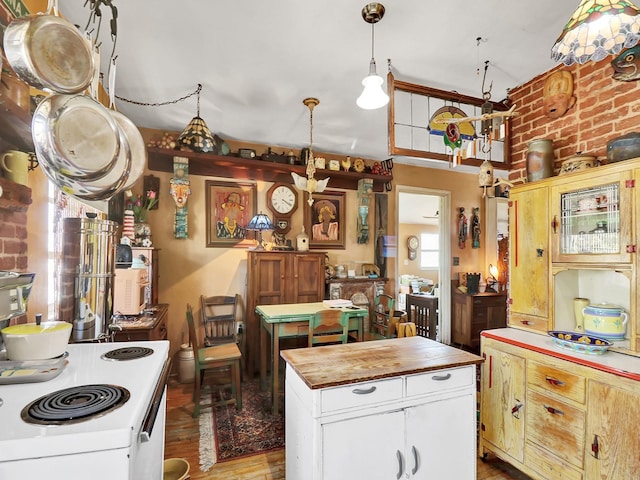 kitchen with wood counters, wood finished floors, a center island, brick wall, and white cabinets