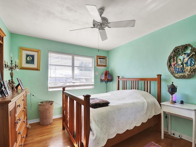 bedroom featuring a wall mounted air conditioner, light wood-type flooring, baseboards, and a ceiling fan