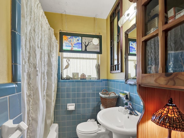 bathroom with a sink, toilet, tile walls, and wainscoting