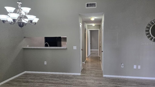 unfurnished dining area featuring a notable chandelier, visible vents, a sink, wood finished floors, and baseboards