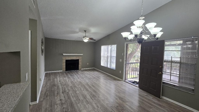 unfurnished living room with baseboards, dark wood finished floors, a tiled fireplace, lofted ceiling, and a textured ceiling