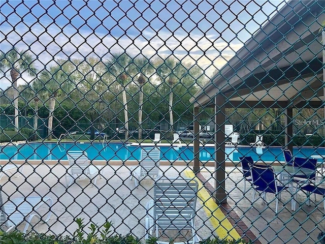 view of swimming pool featuring a tennis court and fence