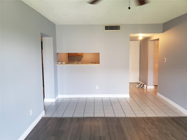 tiled empty room featuring a textured ceiling, visible vents, and baseboards