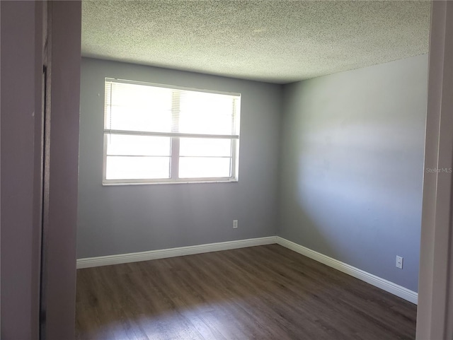 spare room featuring a textured ceiling, dark wood-type flooring, and baseboards