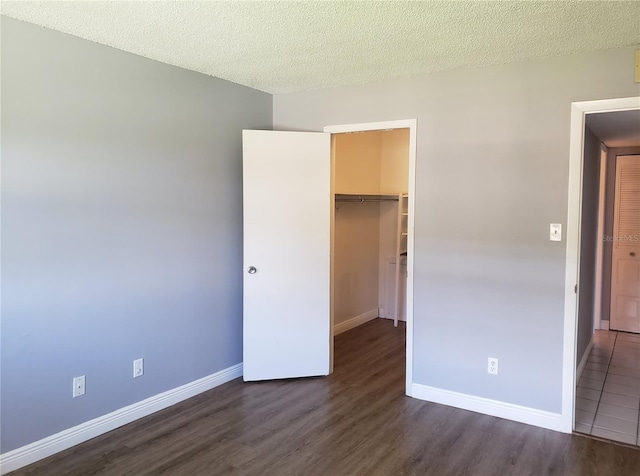 unfurnished bedroom with dark wood-style floors, a closet, a spacious closet, a textured ceiling, and baseboards