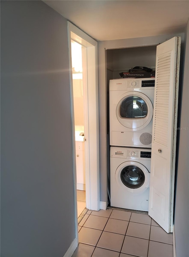 clothes washing area with stacked washer / drying machine, laundry area, tile patterned flooring, and baseboards