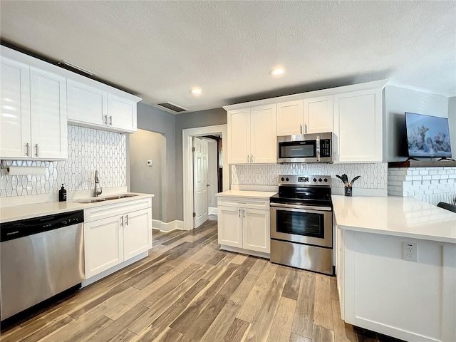 kitchen with visible vents, white cabinets, stainless steel appliances, light wood-type flooring, and a sink