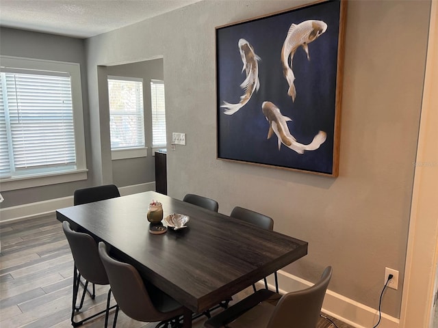 dining room with a textured ceiling, baseboards, and wood finished floors