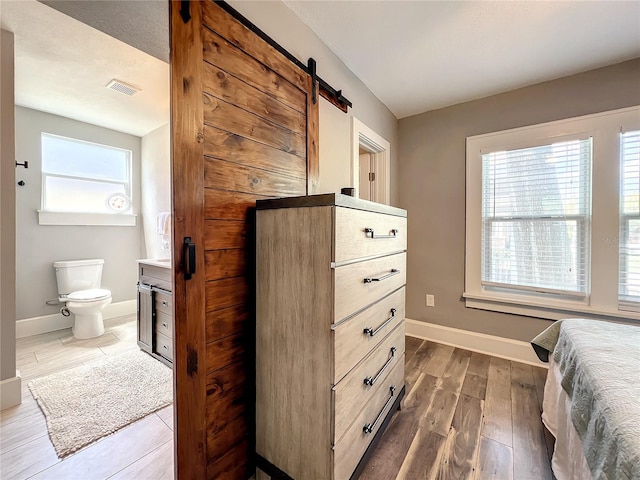 bedroom featuring dark wood-style floors, visible vents, baseboards, and a barn door