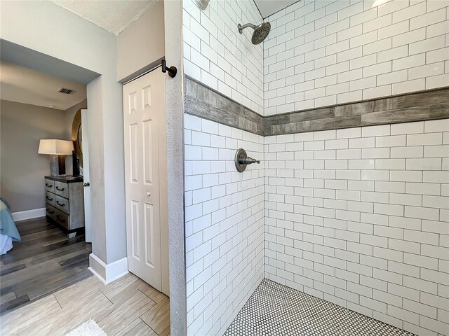 ensuite bathroom featuring tiled shower, wood finished floors, visible vents, and baseboards