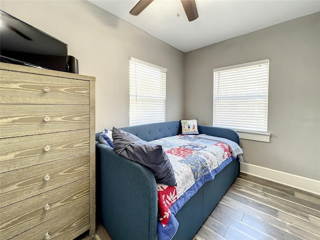 bedroom featuring multiple windows, wood finished floors, a ceiling fan, and baseboards