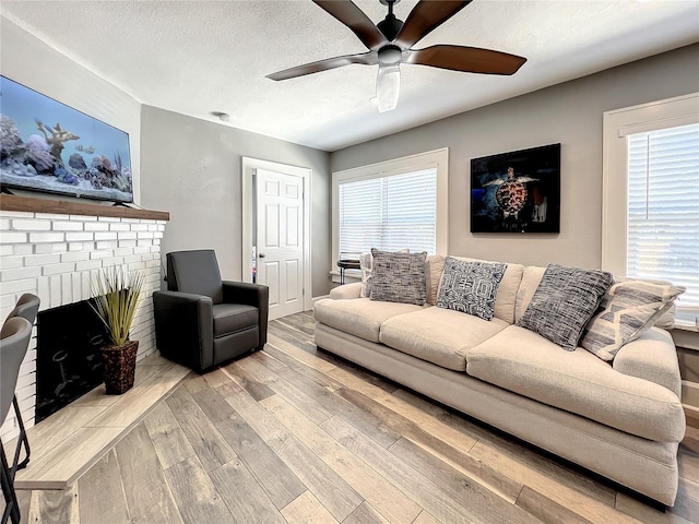 living room featuring a brick fireplace, a textured ceiling, ceiling fan, and wood finished floors