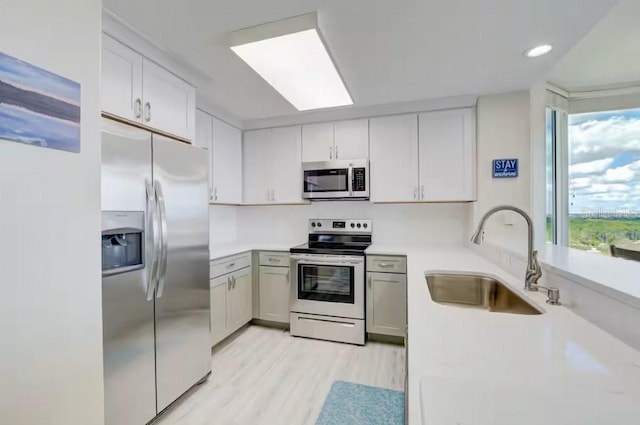 kitchen featuring a skylight, stainless steel appliances, light countertops, light wood-style floors, and a sink