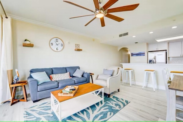 living room featuring arched walkways, crown molding, visible vents, a ceiling fan, and light wood-style floors