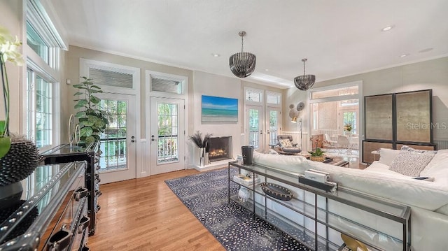 living room with french doors, crown molding, a lit fireplace, and wood finished floors