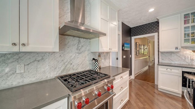 kitchen with wall chimney range hood, white cabinets, wallpapered walls, and stainless steel stove