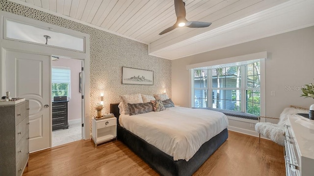 bedroom with crown molding, an accent wall, wood ceiling, light wood-type flooring, and baseboards