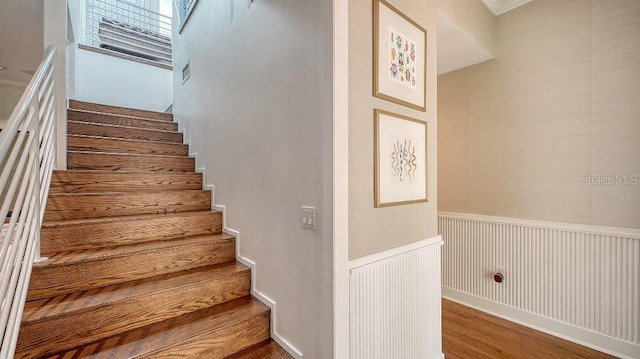 stairway with a wainscoted wall and wood finished floors