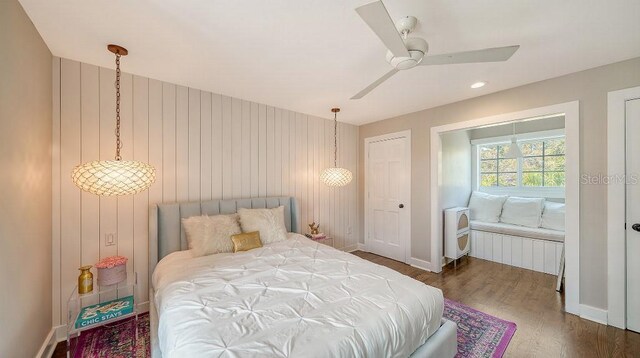 bedroom featuring ceiling fan, wooden walls, baseboards, and wood finished floors