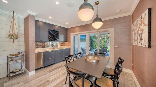 dining area with ornamental molding, wet bar, light wood-type flooring, and baseboards