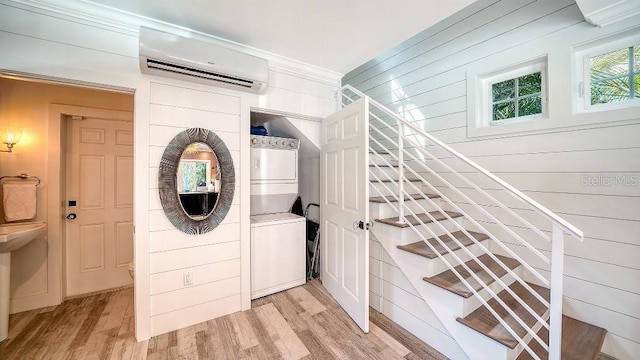 laundry room with laundry area, light wood-style flooring, crown molding, stacked washing maching and dryer, and a wall mounted AC