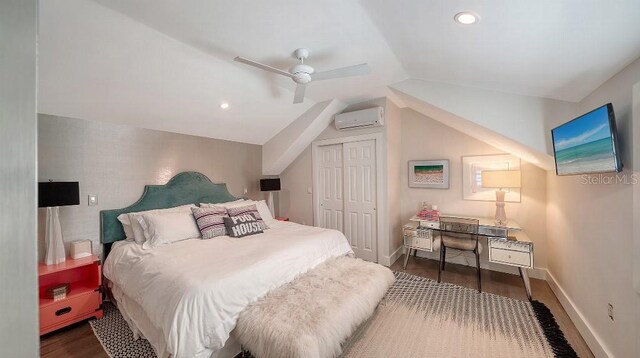 bedroom featuring a wall unit AC, wood finished floors, baseboards, vaulted ceiling, and a closet