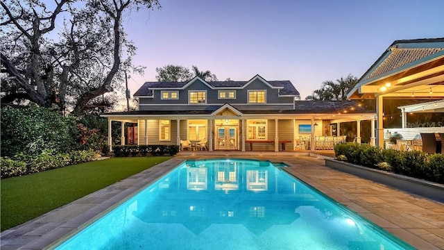 back of house at dusk with a lawn, an outdoor pool, a patio, and french doors