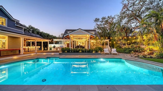 pool at dusk with a patio area and an outdoor pool