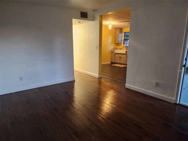 empty room featuring visible vents, baseboards, and dark wood-style flooring