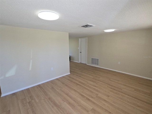 unfurnished room with light wood finished floors, baseboards, visible vents, and a textured ceiling