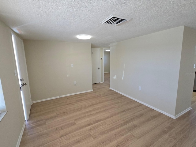 unfurnished room with visible vents, light wood-style flooring, baseboards, and a textured ceiling