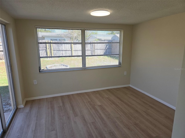 unfurnished room with a textured ceiling, baseboards, and wood finished floors