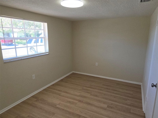 spare room with light wood-style floors, a textured ceiling, and baseboards