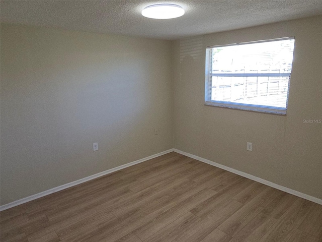 spare room featuring a textured ceiling, baseboards, and wood finished floors