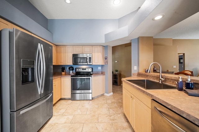 kitchen featuring recessed lighting, a sink, light countertops, appliances with stainless steel finishes, and light brown cabinetry